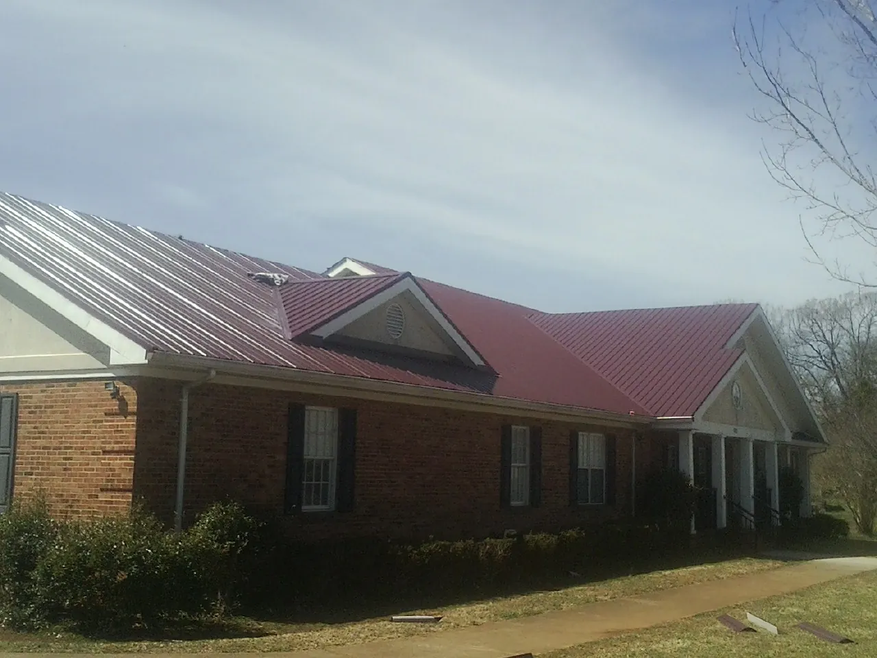 Red metal roof with gabled entries on a long brick building, from a Hail Damage Roof Repair job in Thornton
