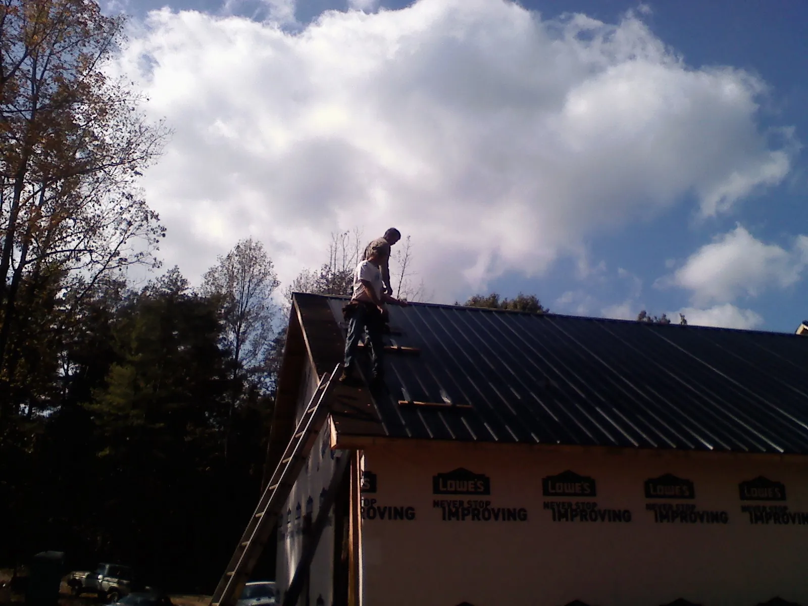 Roofer fastening dark metal panels high against a cloudy sky, from a Roof Inspection job in Thornton